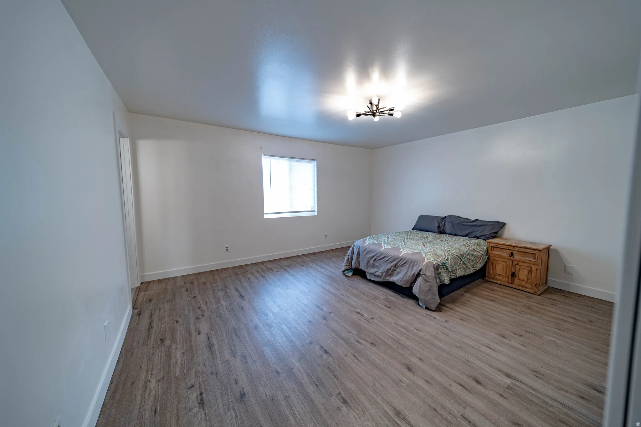 Spacious room featuring wood-finish flooring, white walls, and a modern ceiling light fixture