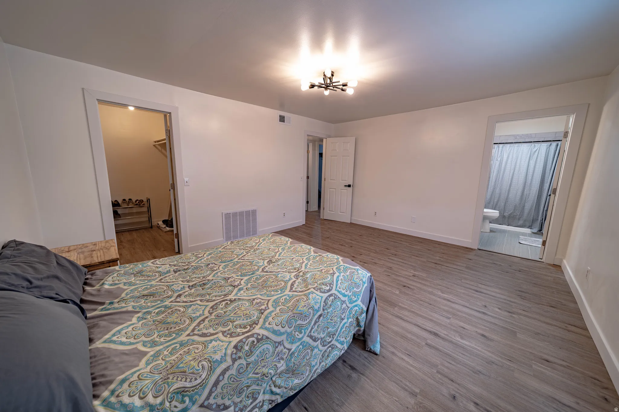 Spacious room featuring wood-finish flooring, white walls, and a contemporary ceiling light fixture
