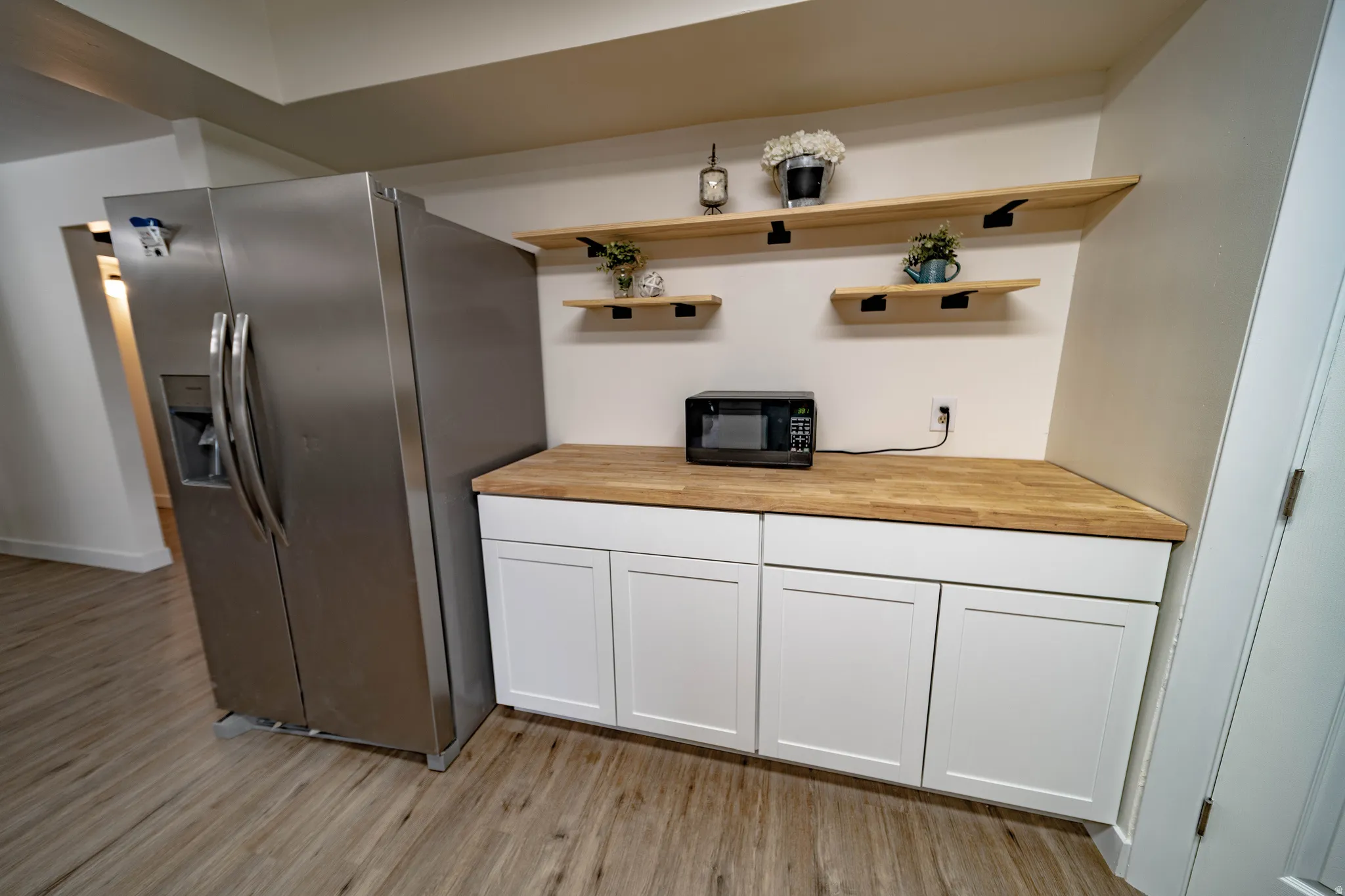 Kitchenette featuring a stainless steel side-by-side refrigerator, white shaker-style cabinetry, wood-finish countertops, and open wood shelving with black metal supports