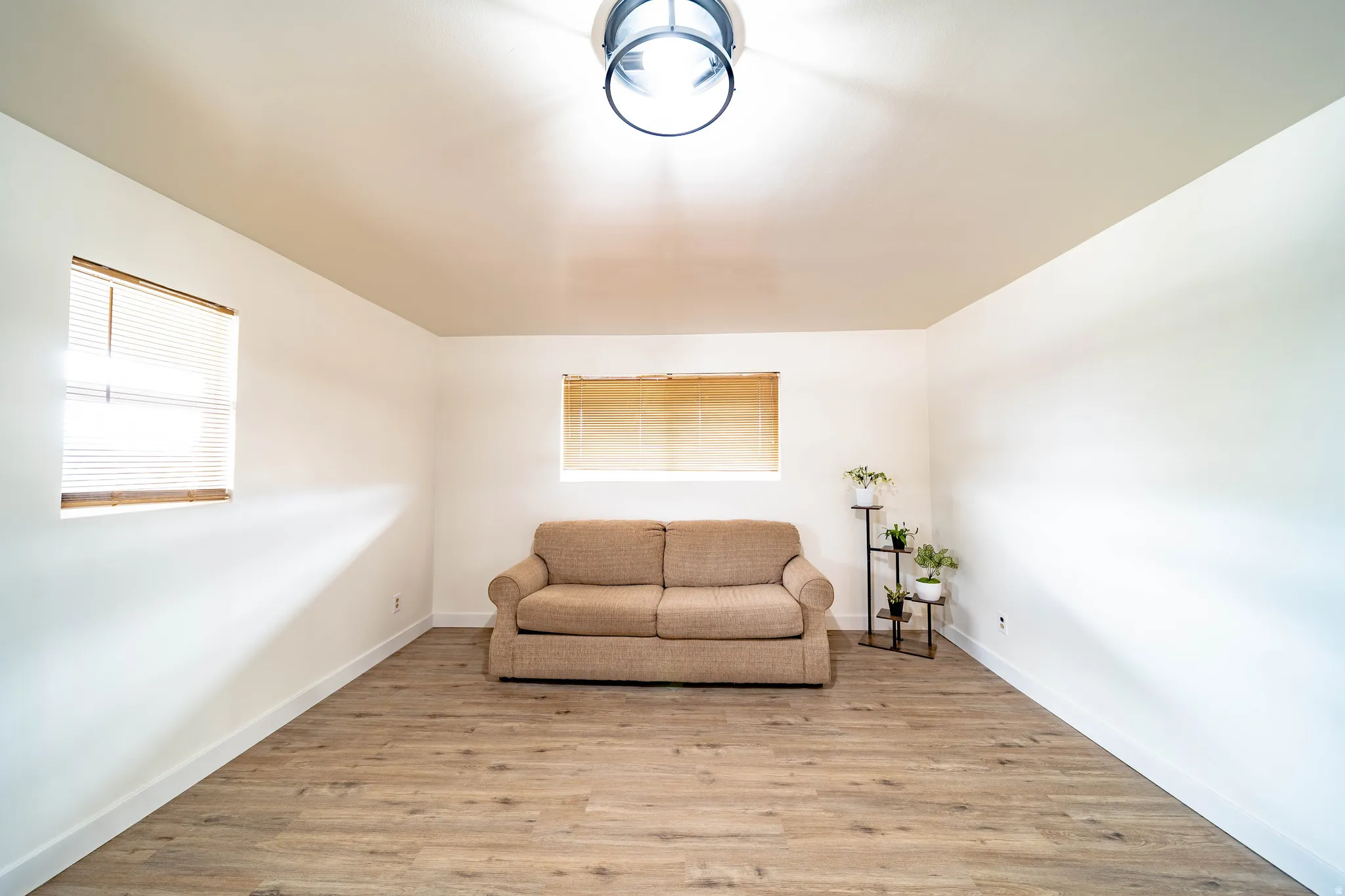 Room featuring wood-finish flooring, two windows with blinds, a ceiling-mounted light fixture, and white painted walls with baseboards