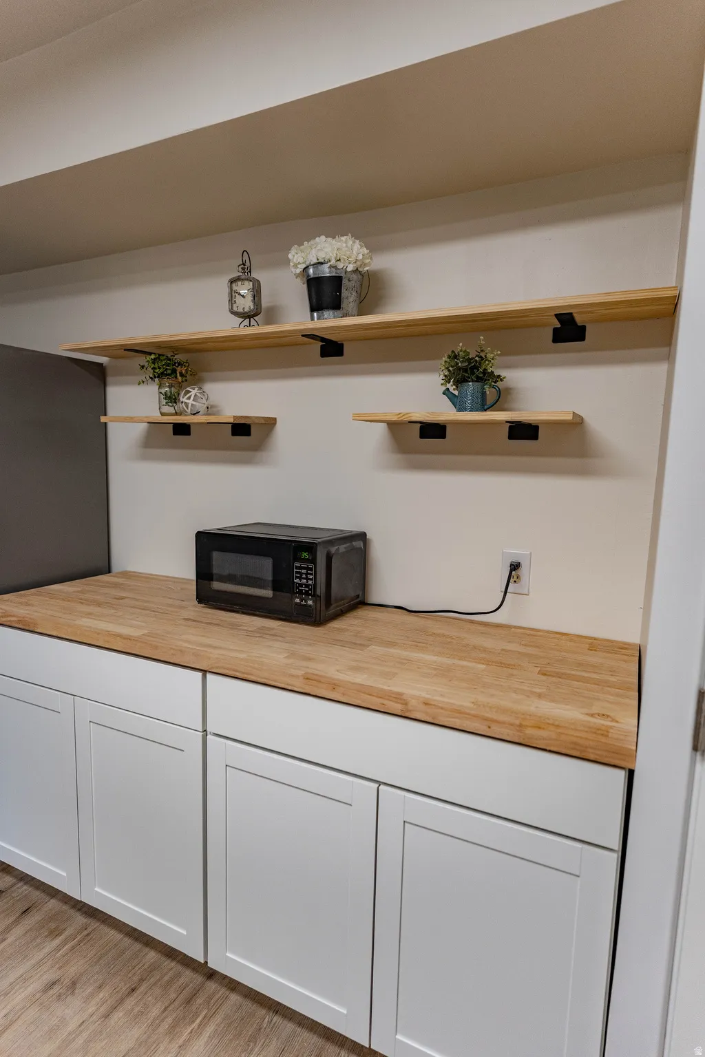 Built-in cabinetry with white shaker-style doors, butcher block countertops, and open wood shelving with black metal brackets