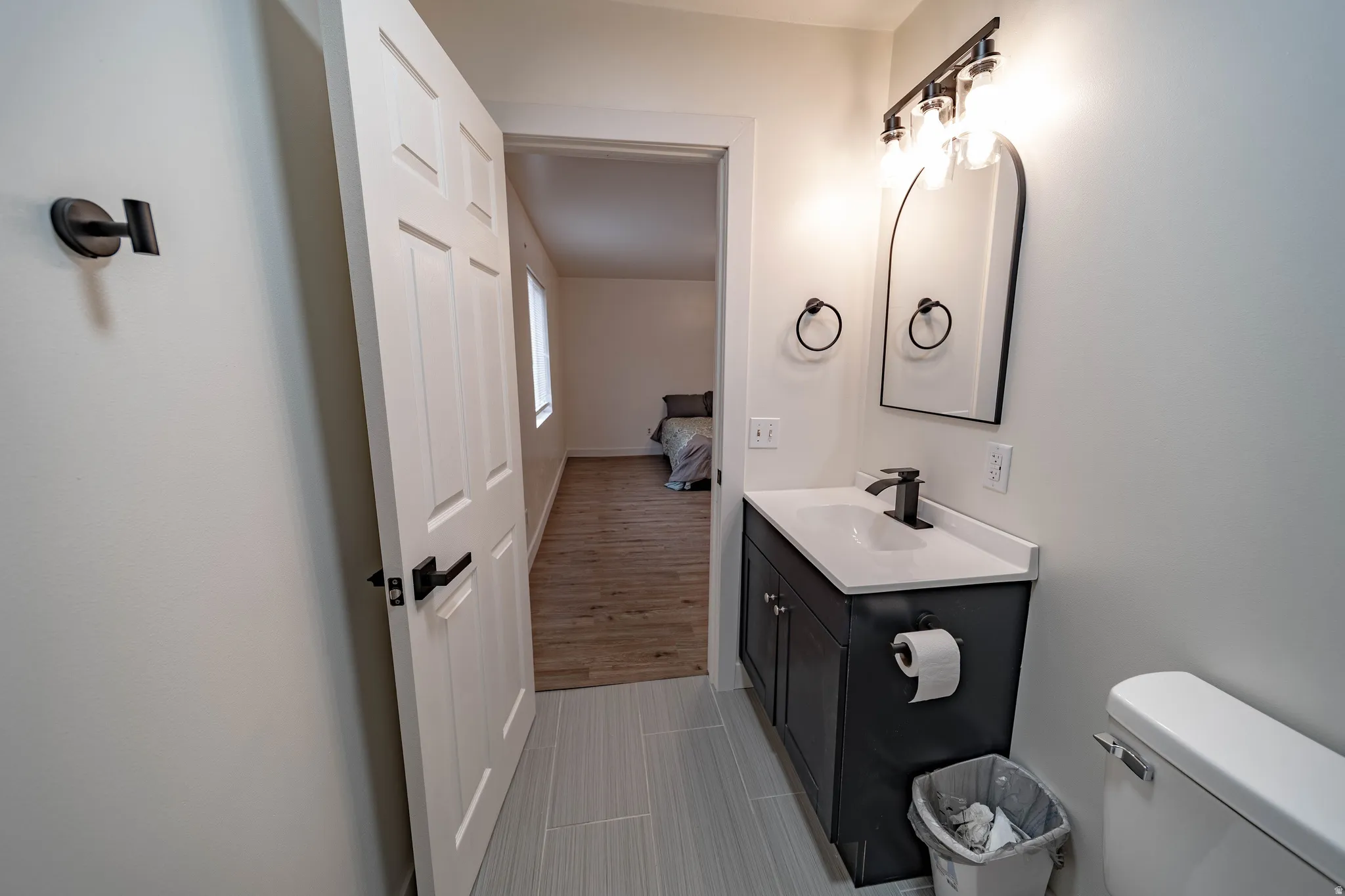 Bathroom featuring a dark vanity with white countertop, arched mirror, and matte black fixtures