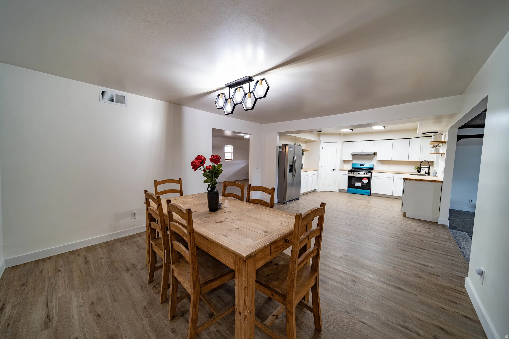 Open-concept living space featuring wood-finish flooring, a modern hexagonal chandelier, and white walls