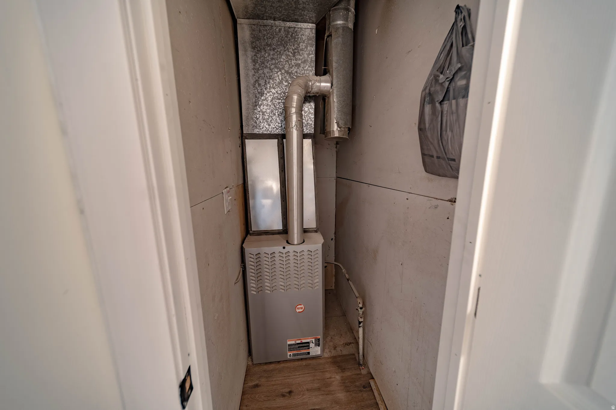 Dedicated utility closet housing a furnace unit with exposed ductwork and a wooden floor