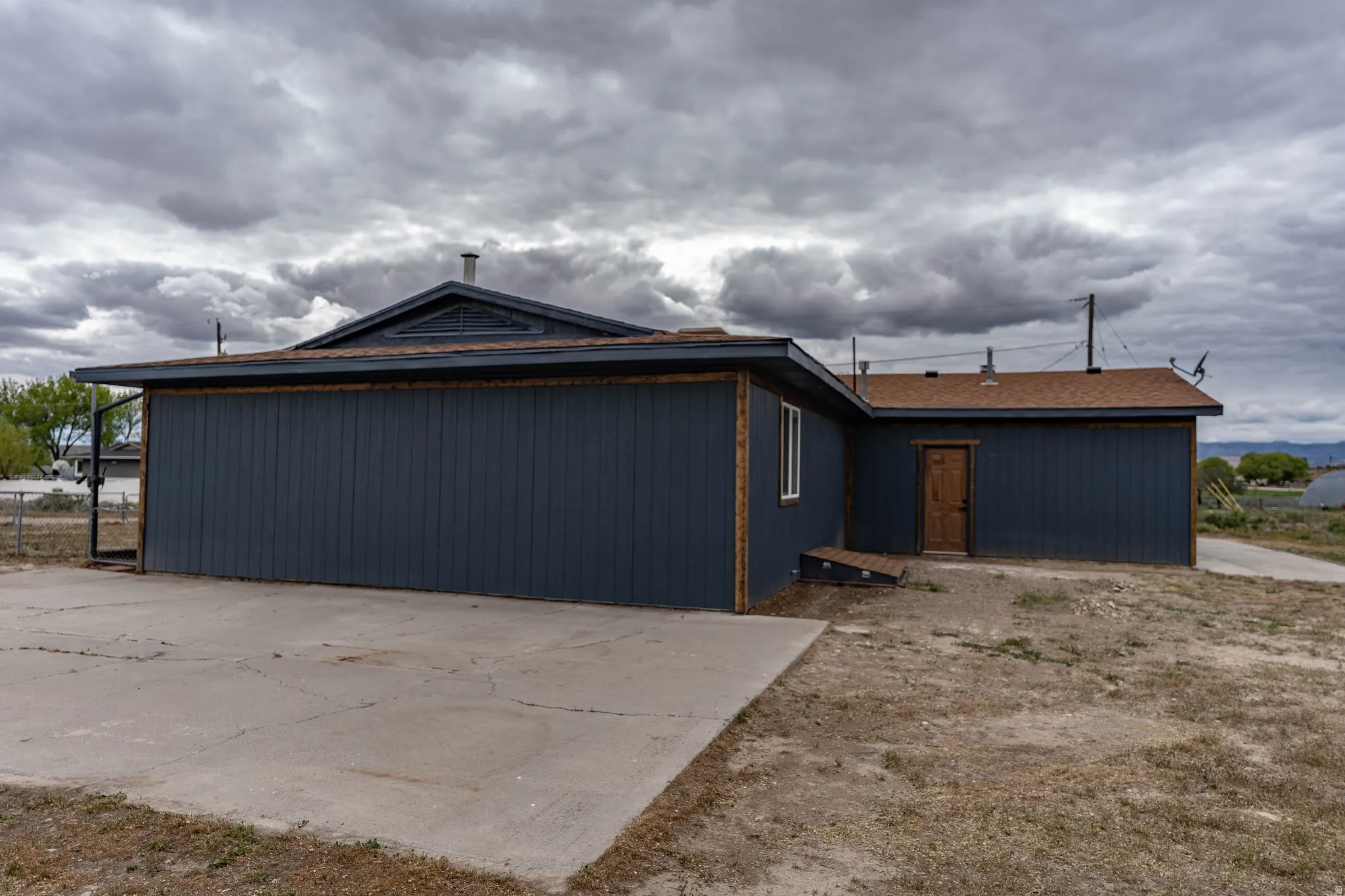 Exterior featuring dark blue siding, brown shingle roofing, a concrete pad, and a light wood-finish door