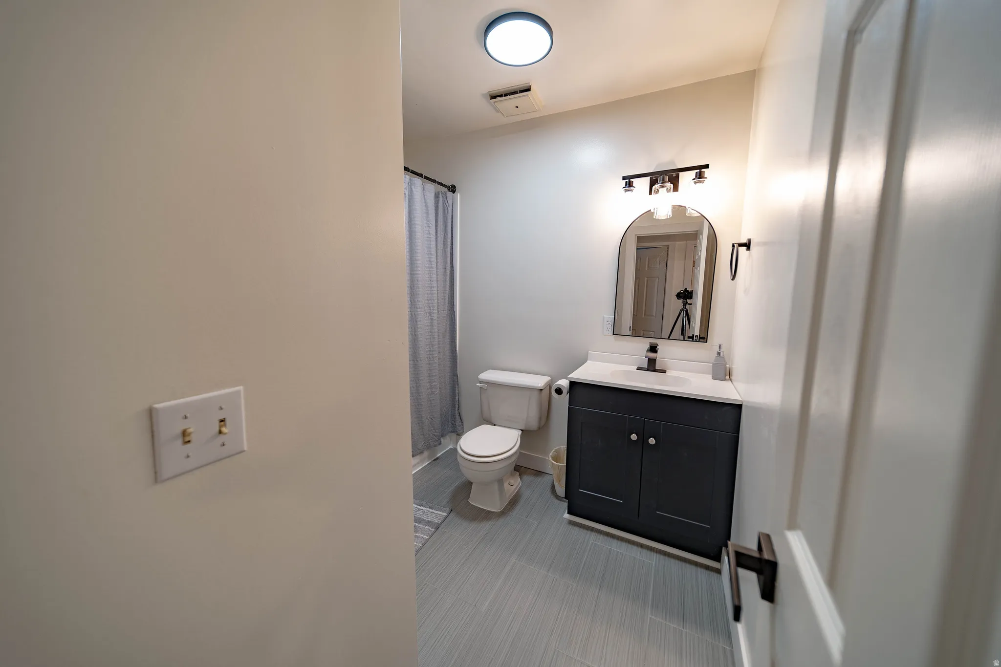 Bathroom featuring a dark wood-finish vanity with white countertop, arched mirror, and contemporary light fixture