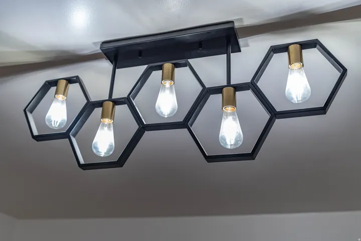 Ceiling-mounted light fixture featuring five hexagonal frames in matte black, each housing an Edison-style bulb with a brass-finish socket