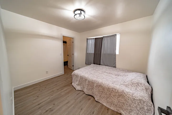 Room featuring wood-finish flooring, white walls, a flush-mount ceiling light, and a window with sheer and blackout curtains
