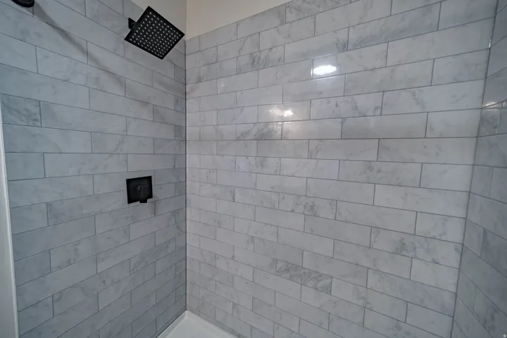 Shower featuring light-toned rectangular tile surround, a matte black rainfall showerhead, and a matte black wall-mounted control fixture