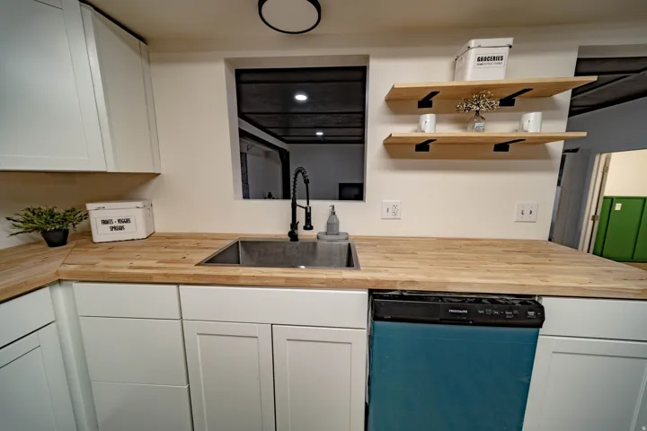 Kitchen workstation featuring a stainless steel sink with a matte black faucet, butcher block countertops, shaker-style white cabinetry, and open shelving