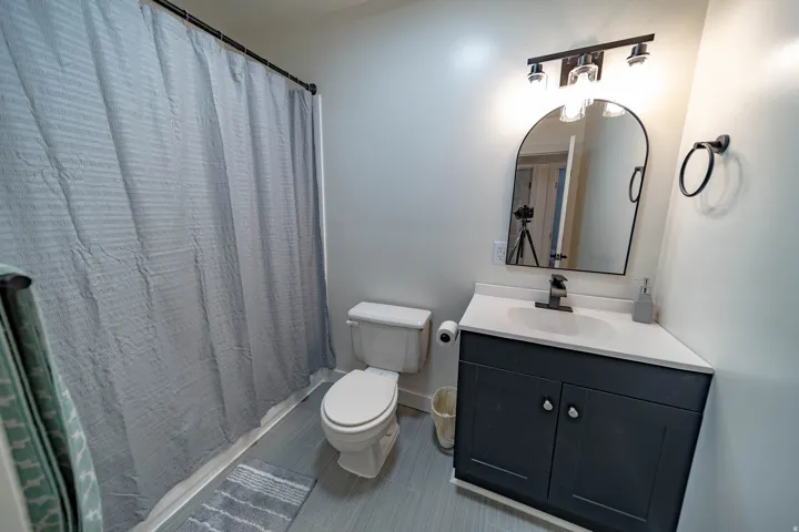 Bathroom vanity with a dark wood-finish cabinet, white countertop, and a contemporary arched mirror
