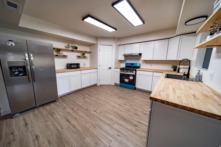 Contemporary kitchen featuring wood-finish flooring, white cabinetry, butcher block countertops, stainless steel appliances, and a black gooseneck faucet