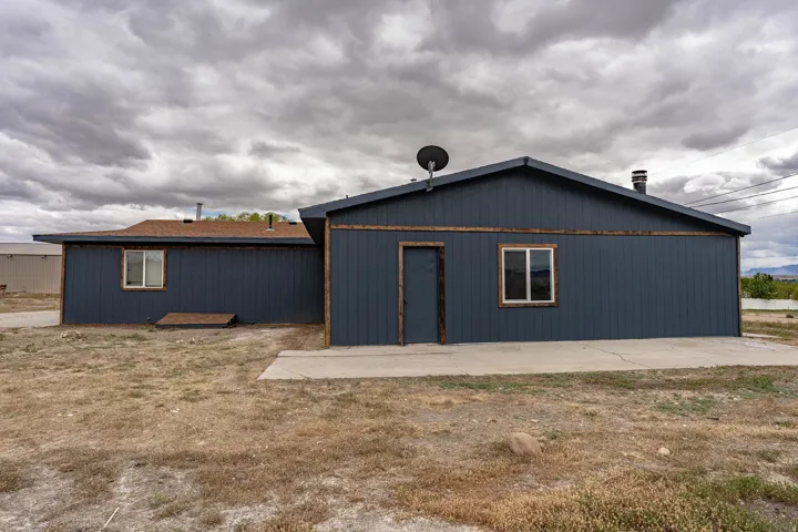 Dark blue vertical siding exterior with natural wood trim accents, multiple windows, and a concrete patio