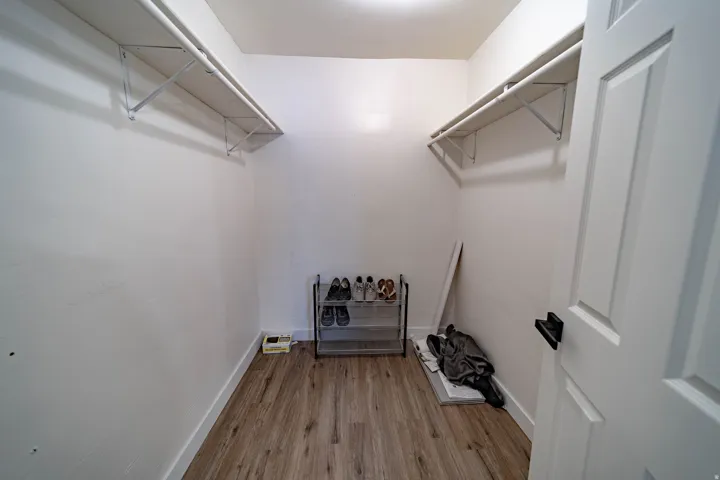 Spacious closet featuring wood-finish flooring, white baseboards, and two levels of built-in shelving with hanging rods
