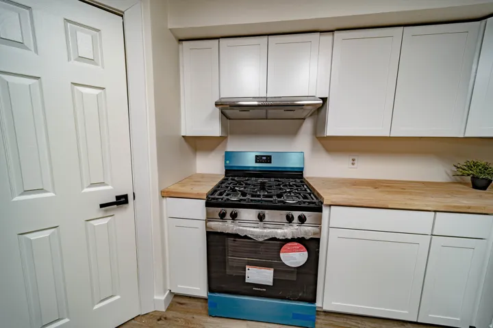Kitchen featuring a stainless steel range with a ventilation hood, white shaker-style cabinetry, and wood-finish countertops
