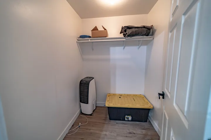 Interior closet featuring white walls, wood-finish flooring, and a white interior door with black hardware