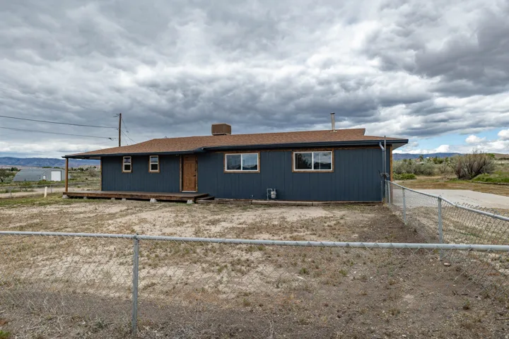 Ranch-style residence featuring a dark blue exterior siding, a light brown shingle roof, and a wood-finish front door
