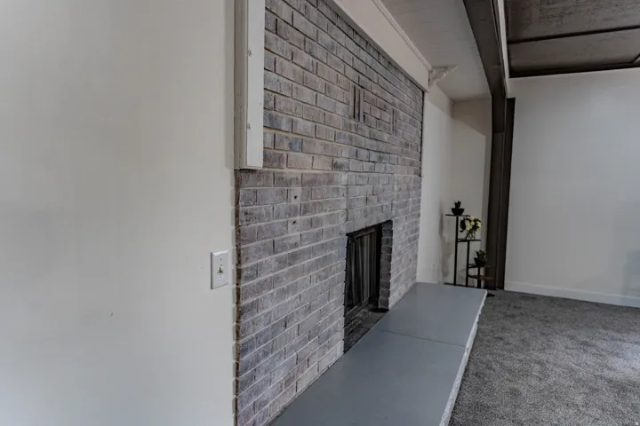 Brick fireplace with a stone hearth, white walls, and carpet flooring