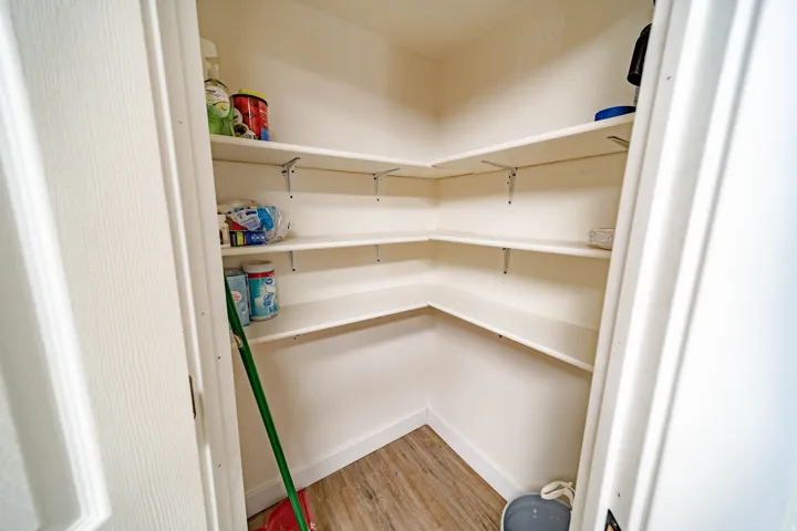 Walk-in pantry featuring multiple levels of white shelving, wood-finish flooring, and white baseboards