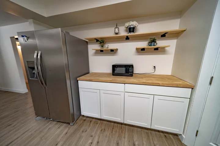 Kitchenette featuring a stainless steel side-by-side refrigerator, white shaker-style cabinetry, wood-finish countertops, and open wood shelving with black metal supports