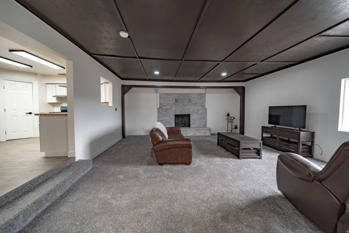Spacious living area featuring a coffered ceiling, light gray carpeting, and a stone-front fireplace