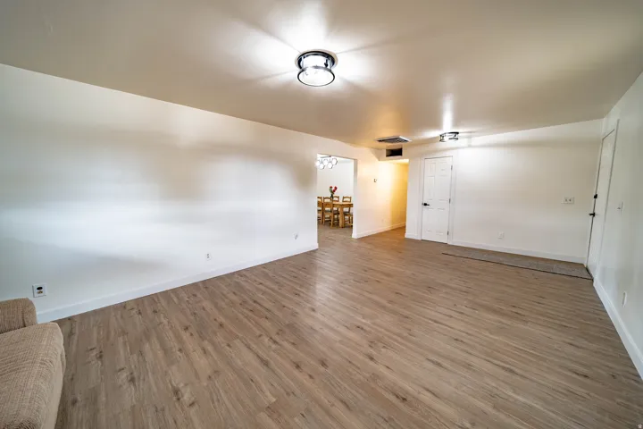 Spacious room featuring wood-finish flooring, white walls, white baseboards, and two flush-mount ceiling lights