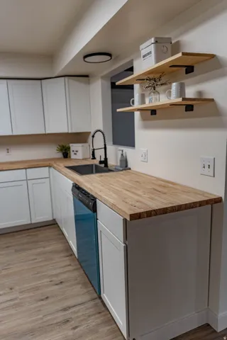 Kitchen featuring crisp white cabinetry, wood-finish countertops, stainless steel undermount sink with a matte black gooseneck faucet, a built-in dishwasher, and open wood shelving