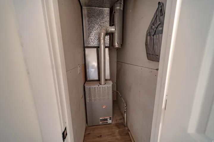 Dedicated utility closet housing a furnace unit with exposed ductwork and a wooden floor