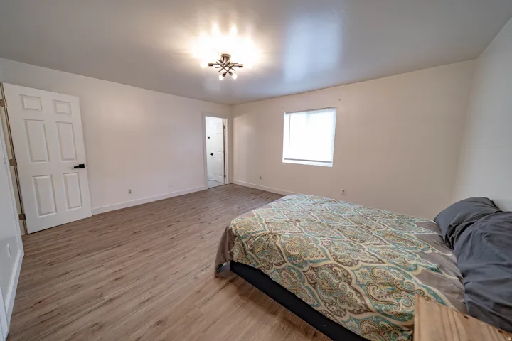 Spacious room featuring wood-finish flooring, white walls, and a modern ceiling light fixture