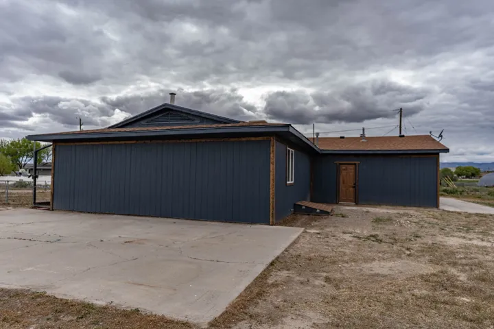 Exterior featuring dark blue siding, brown shingle roofing, a concrete pad, and a light wood-finish door