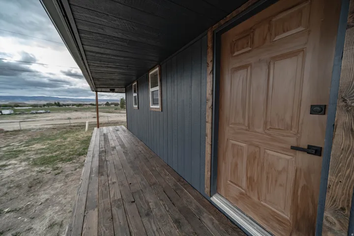 Wood-finish porch featuring a paneled door with matte black hardware, dark siding, and multiple windows