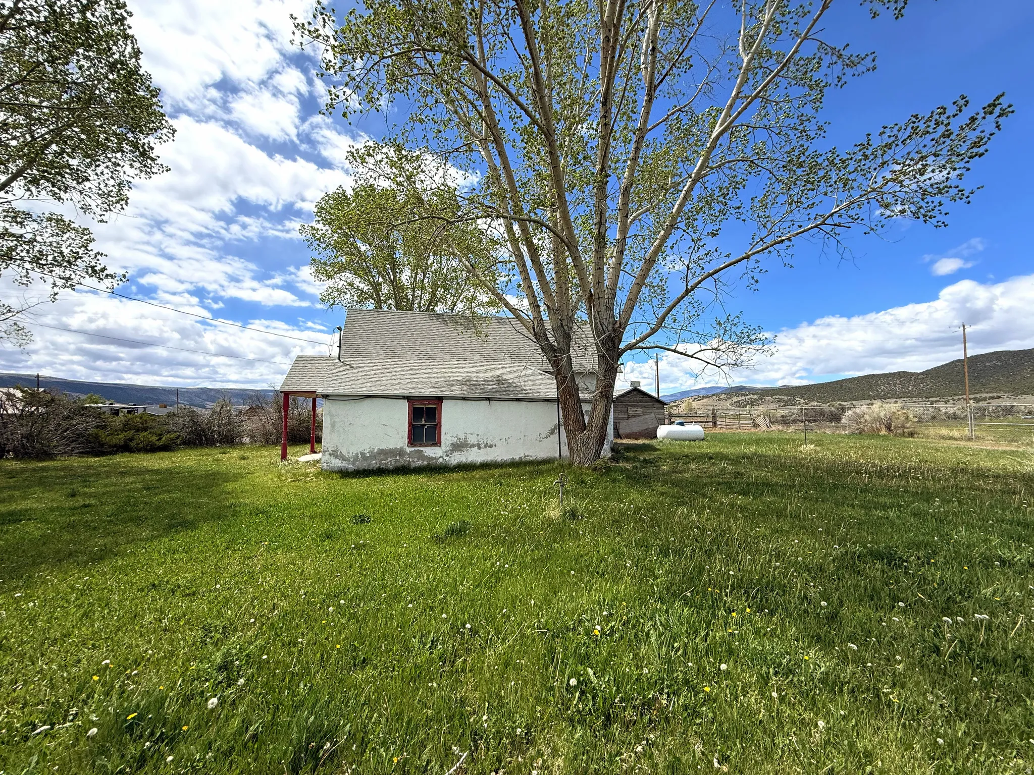 Rural property featuring a white exterior, red-trimmed windows, and a gray shingle roof