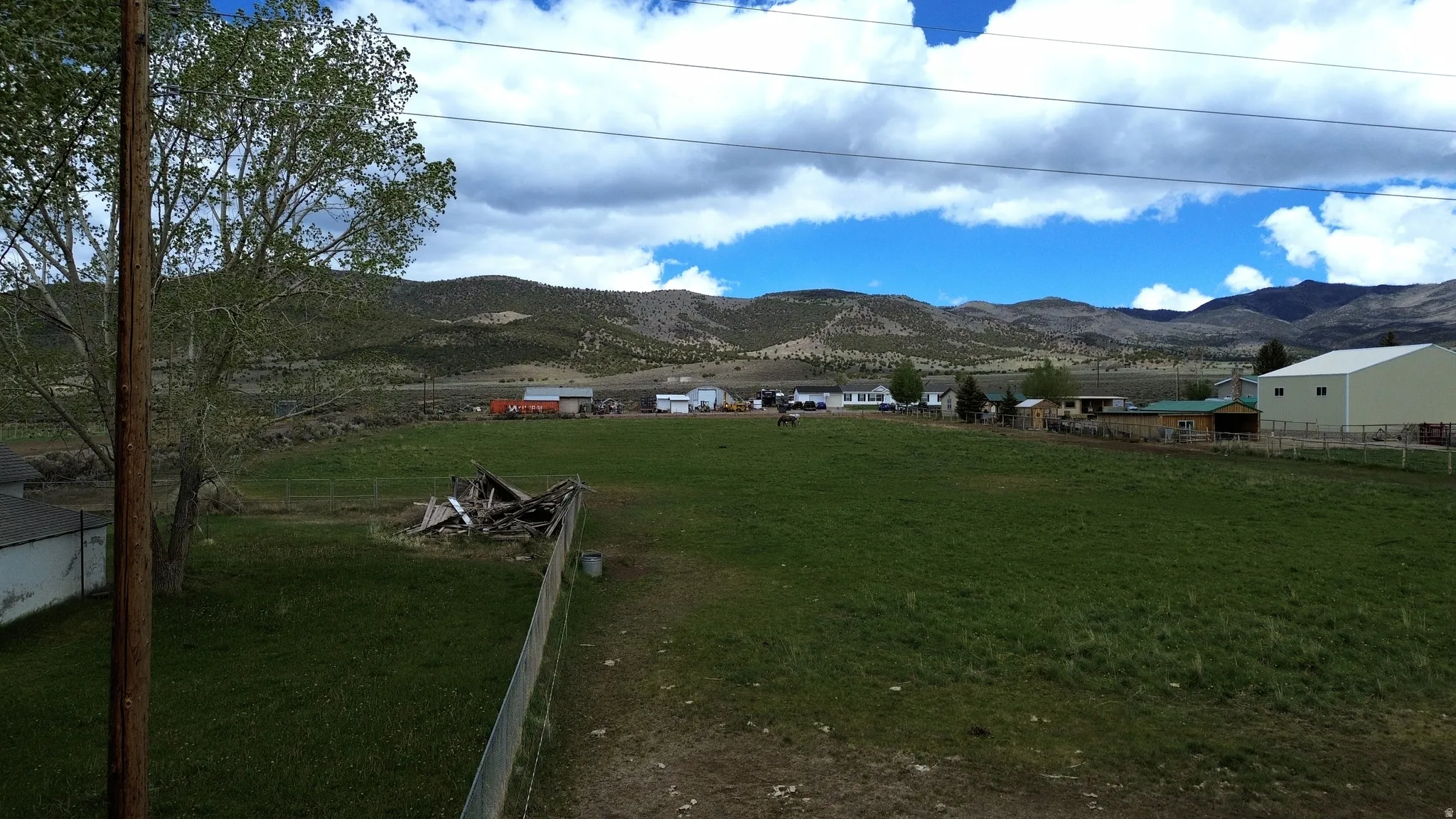 Expansive green field with distant mountain backdrop, featuring scattered residential structures and agricultural buildings