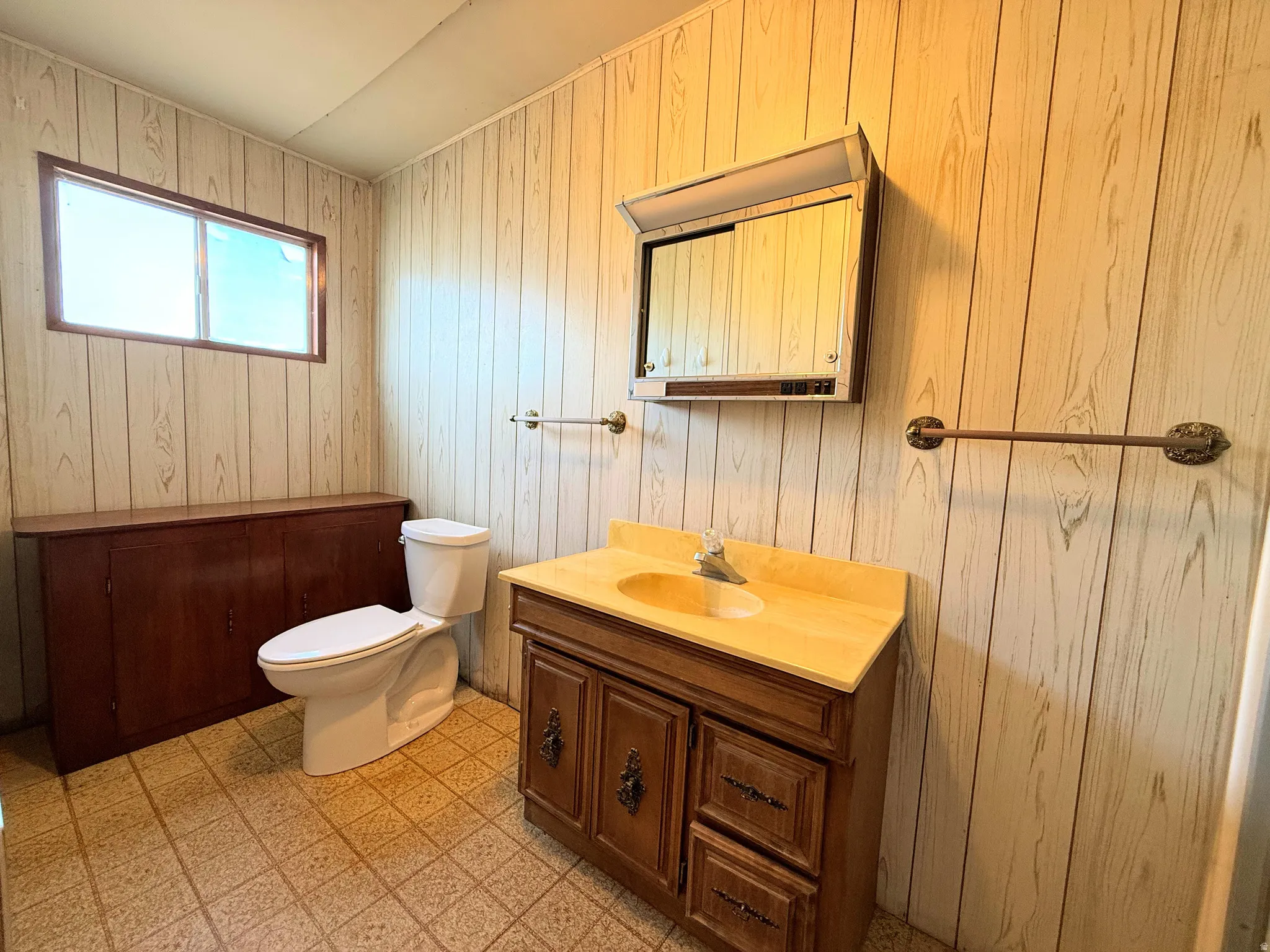 Bathroom featuring wood-grain wall paneling, a white toilet, and a vanity with a built-in sink