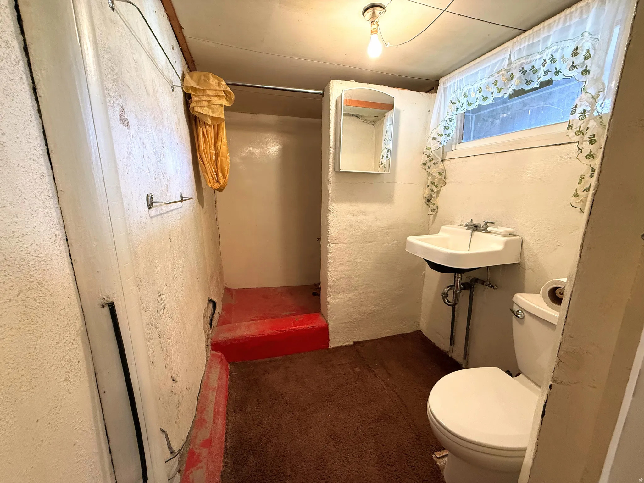 Bathroom featuring a wall-mounted sink, toilet, and shower stall with red-painted floor