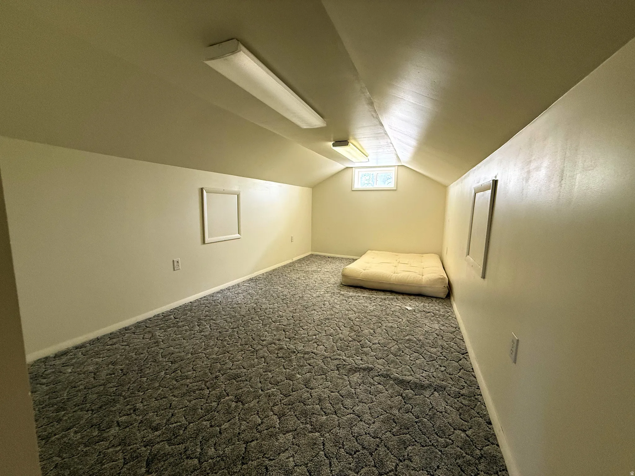 Attic space featuring sloped ceilings, a window, and recessed fluorescent lighting