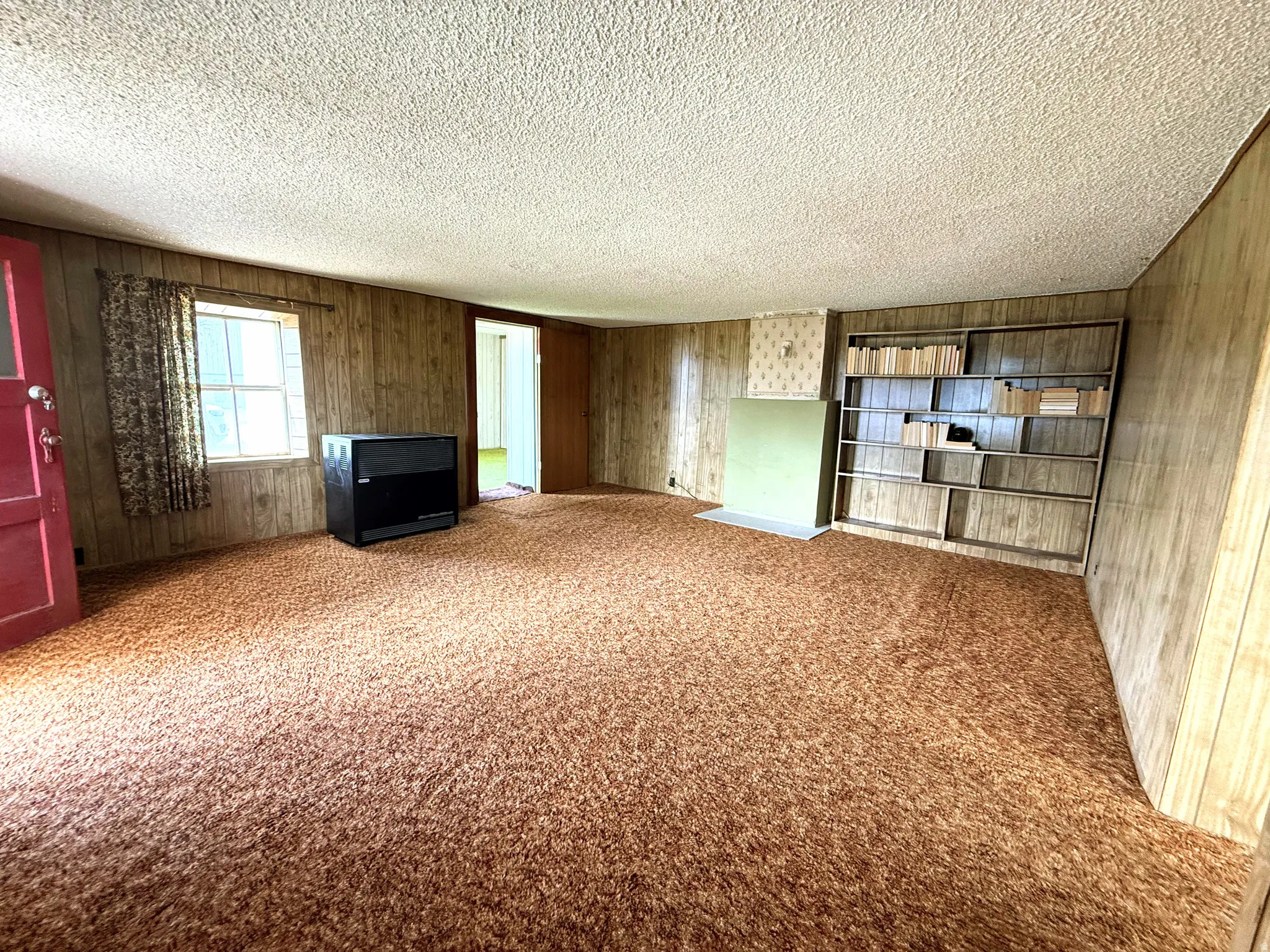 Spacious room with wood-paneled walls, textured ceiling, and plush carpeting