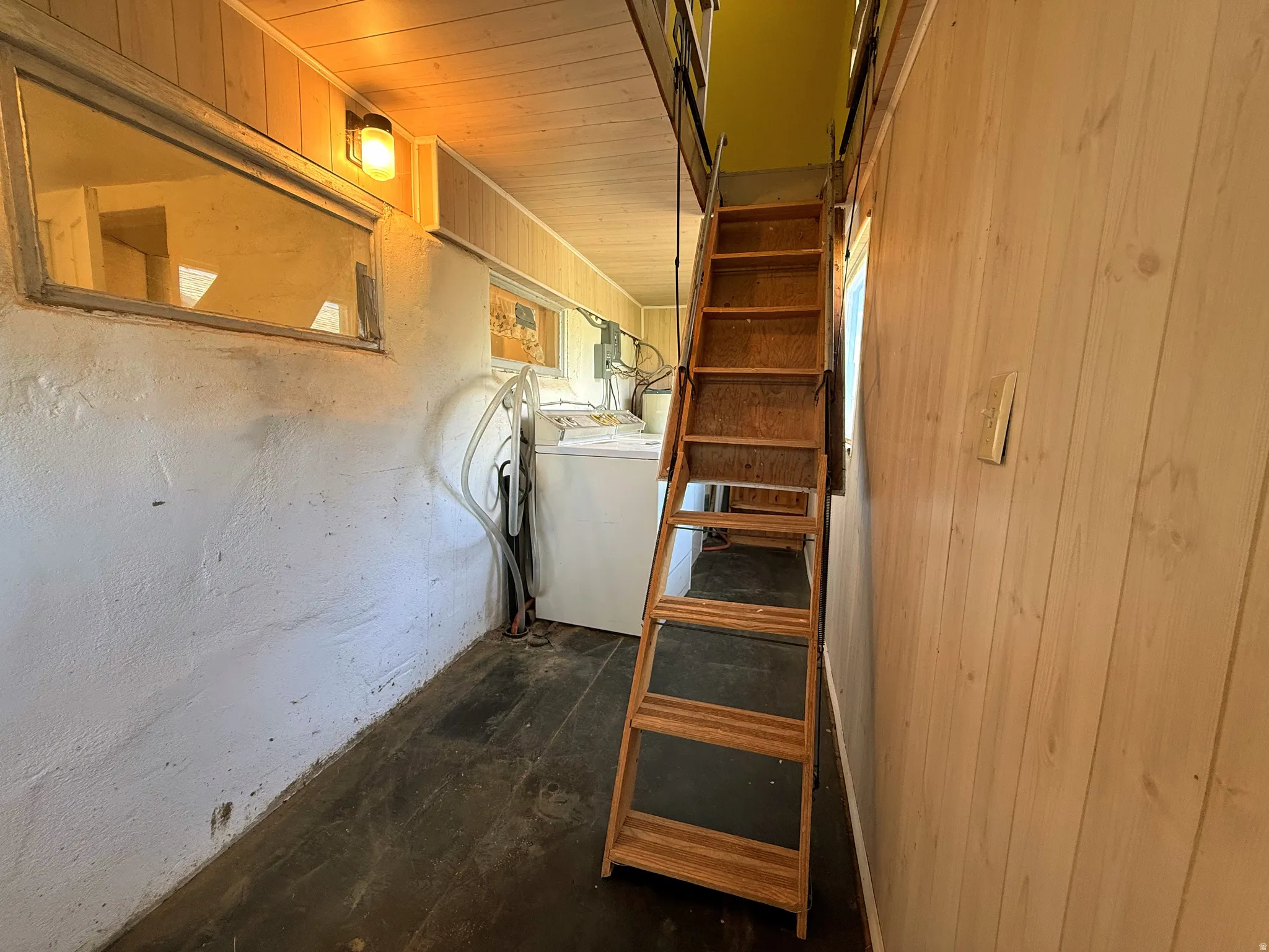 Wooden ladder access to an upper level, featuring wood-finish flooring, a white textured wall, and vertical wood paneling