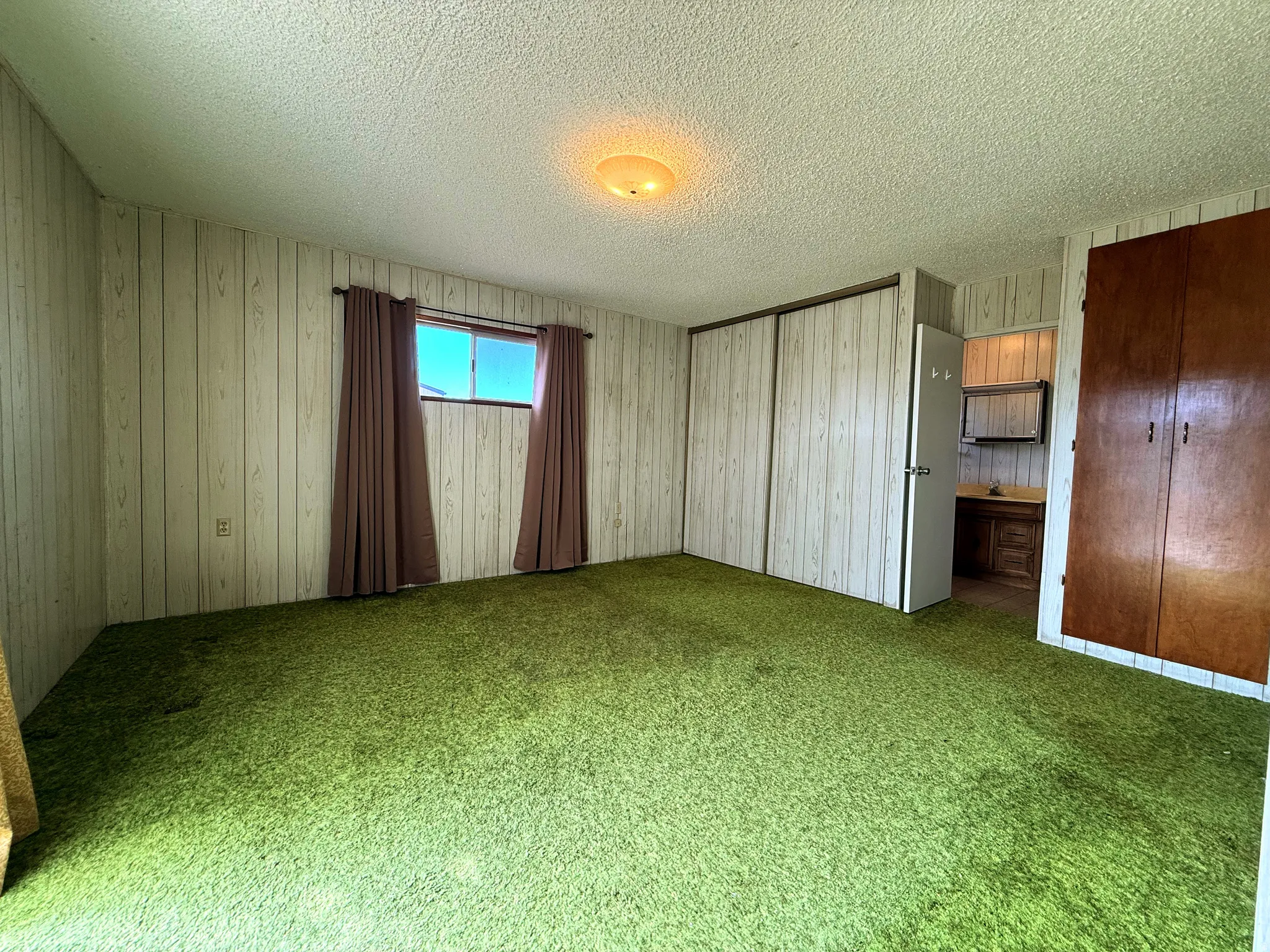 Spacious room featuring green carpet flooring, wood-finish wall paneling, and a window with drapes