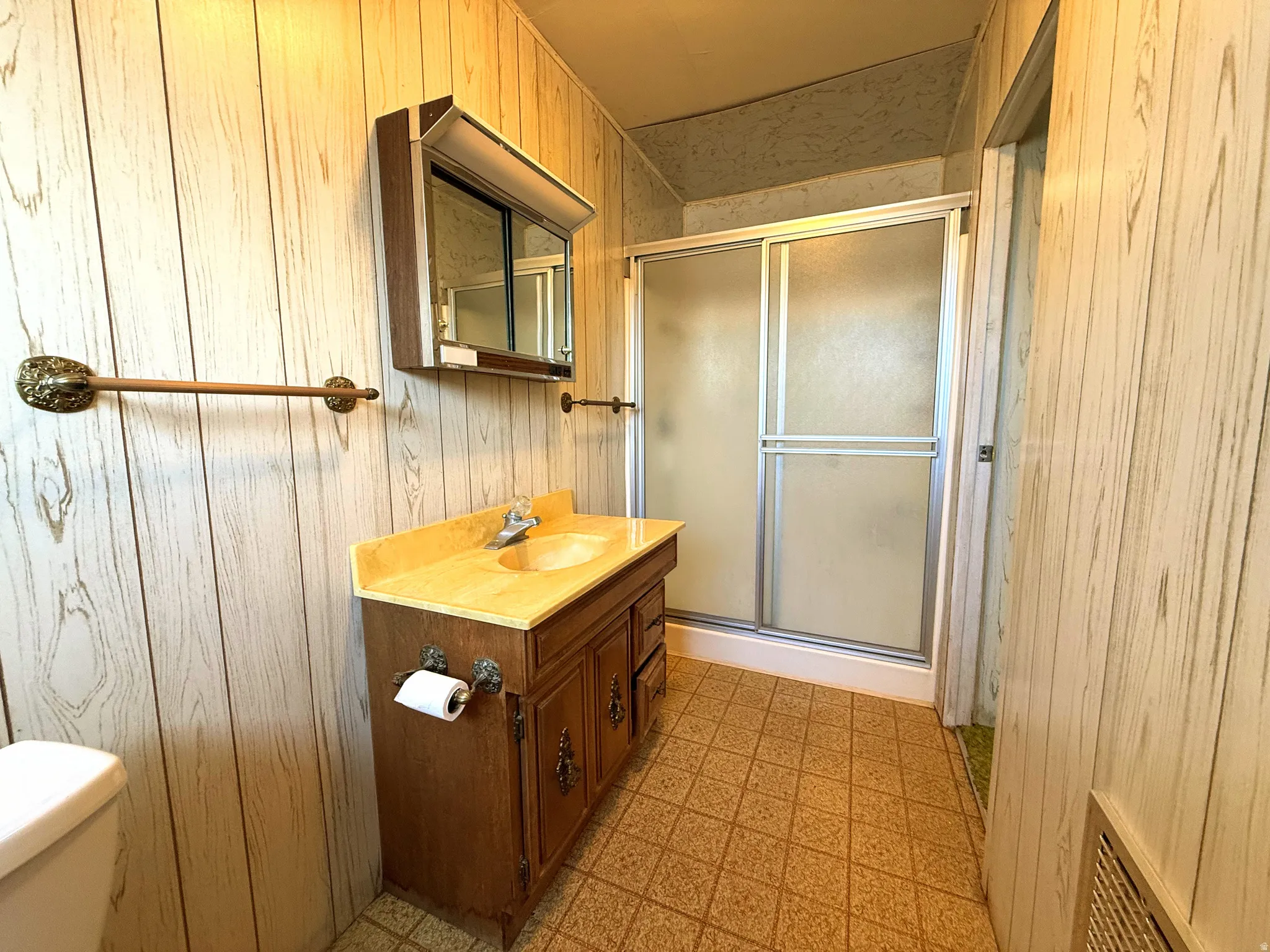 Bathroom featuring wood-finish paneling, a single vanity with a light-toned countertop, and a shower enclosure with frosted sliding doors