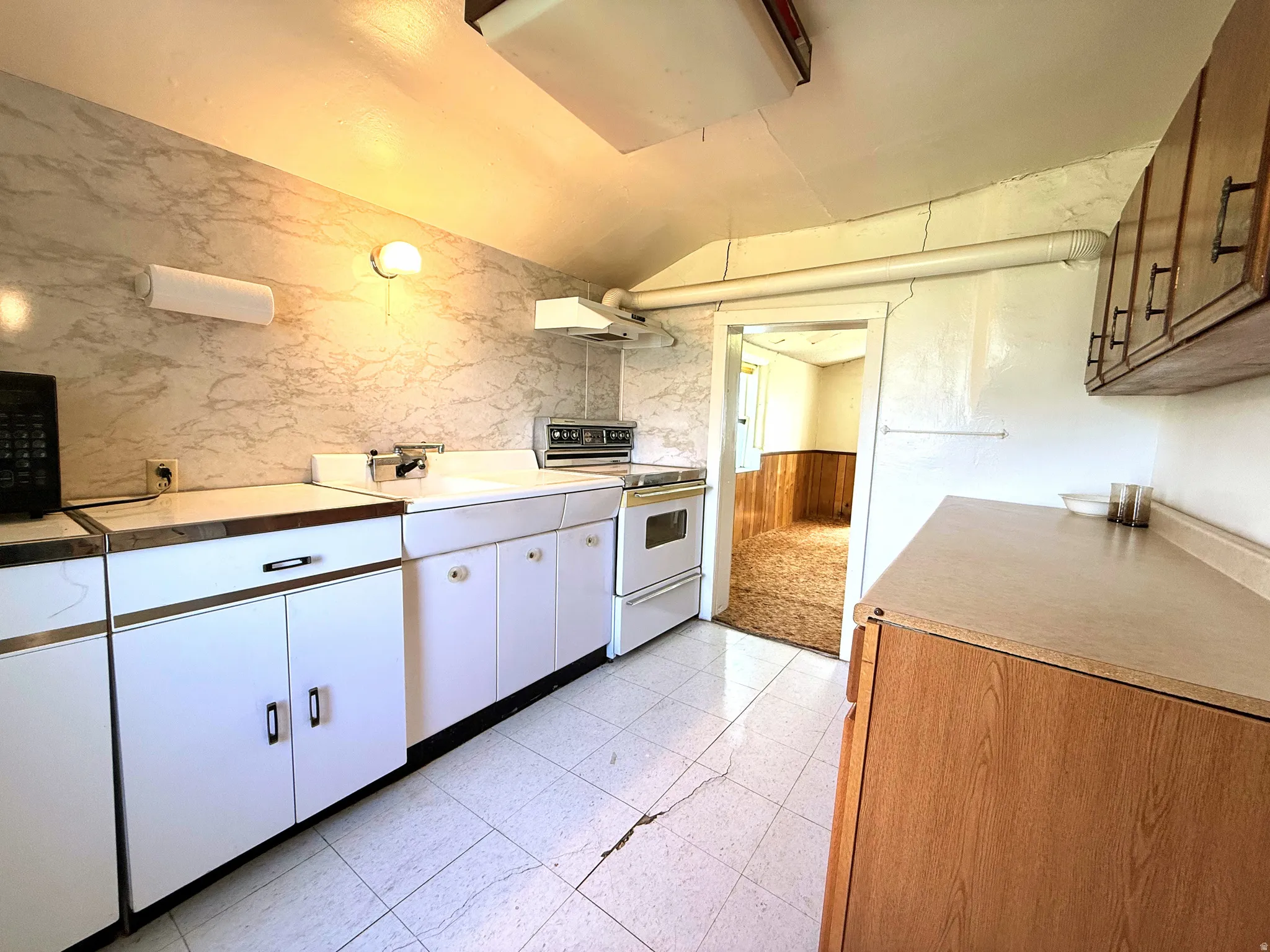 Kitchen featuring white base cabinetry with metal hardware, a wall-mounted light fixture, and a white tiled floor