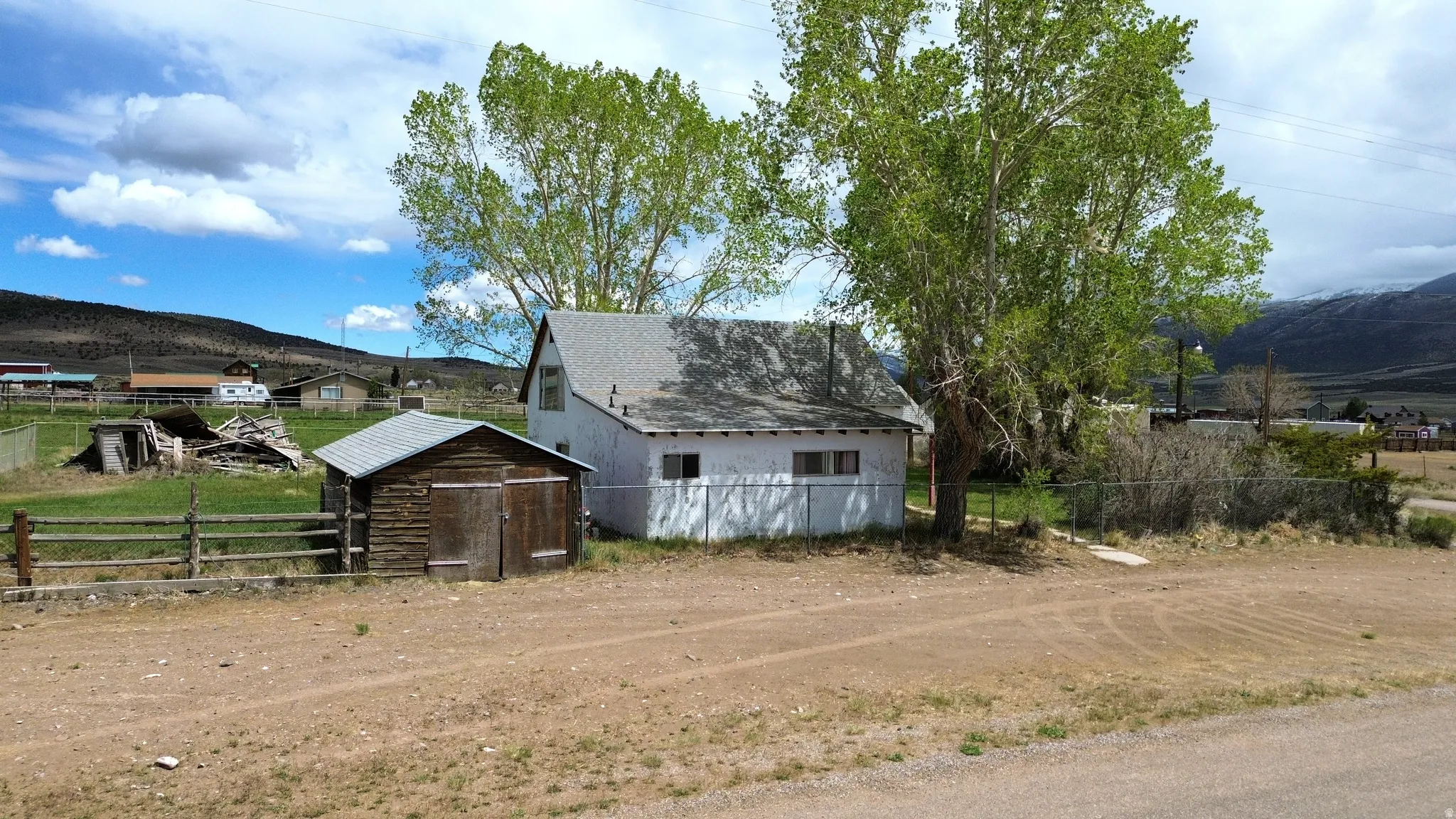 White-sided structure with a gray shingled roof, featuring several windows, and a smaller log-style outbuilding with a gray roof
