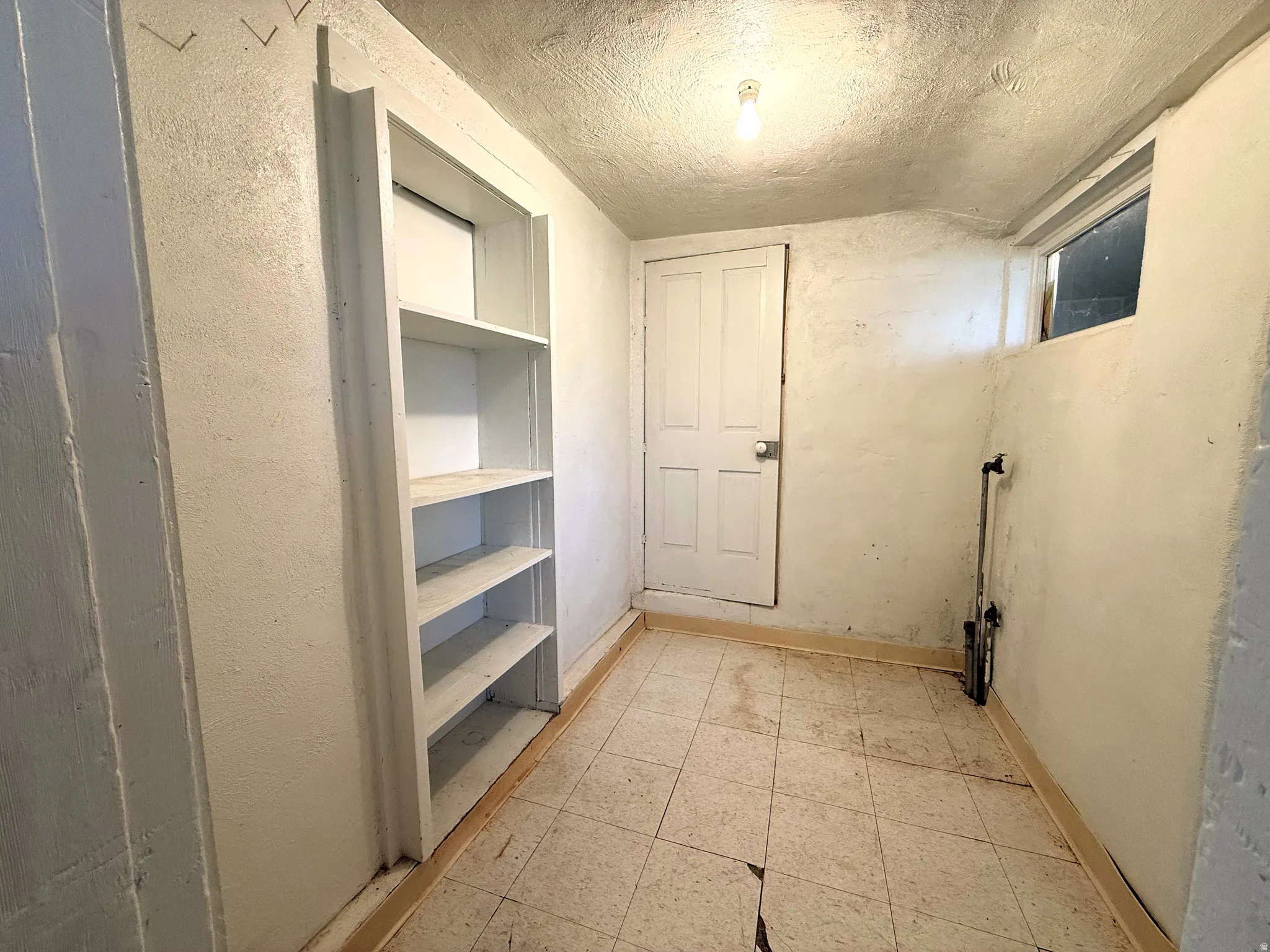 Utility room featuring built-in shelving, a single panel door, a small window, and tile flooring