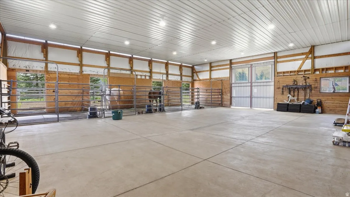Spacious barn interior featuring concrete flooring, exposed wood beam construction, multiple stalls with metal gates, corrugated metal ceiling, and recessed lighting