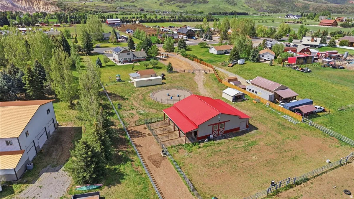 Large red-roofed barn with sliding wood doors, surrounded by fenced pasture and a circular pen