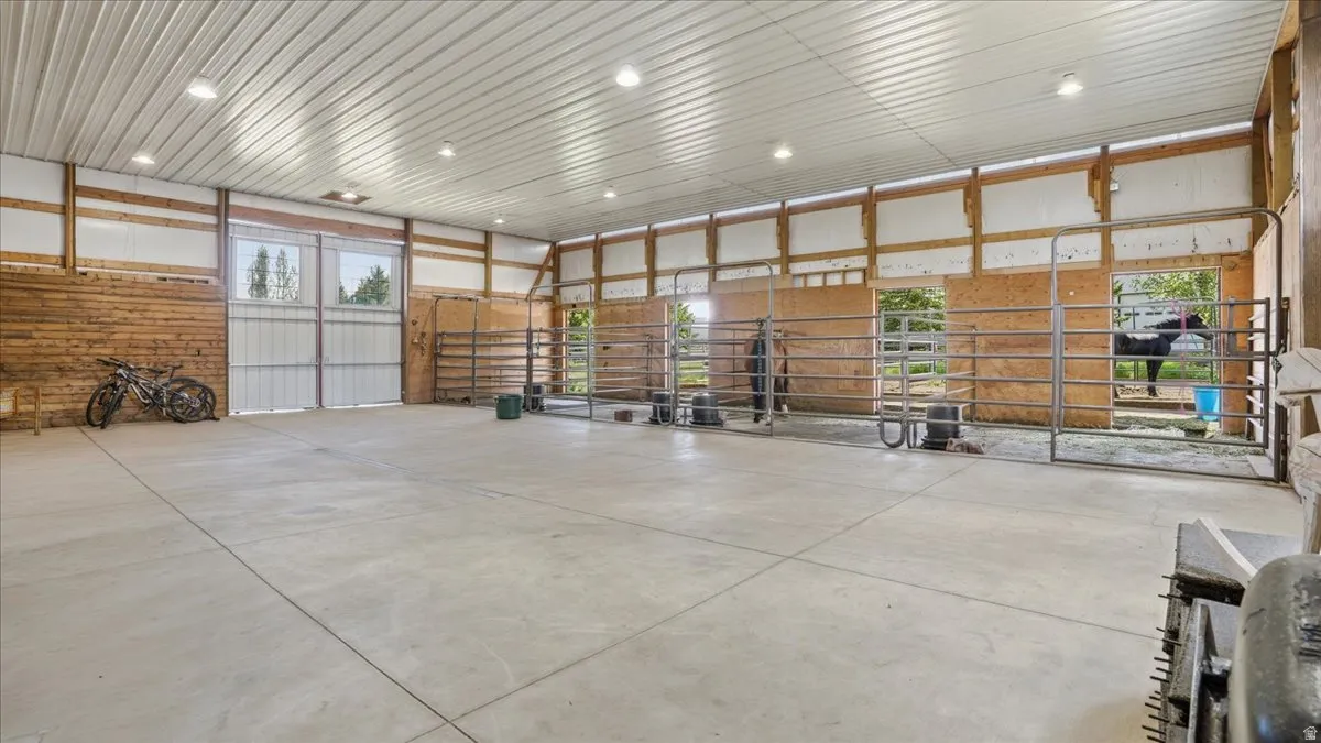 Spacious interior barn featuring a concrete floor, a metal ceiling, multiple stalls with metal gates, and large double-door entry