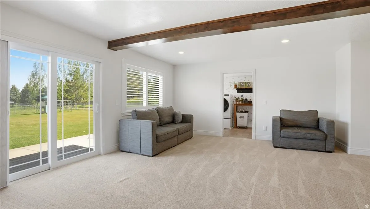 Spacious interior room featuring light-toned carpet, a prominent exposed wood beam, recessed lighting, and white plantation shutters