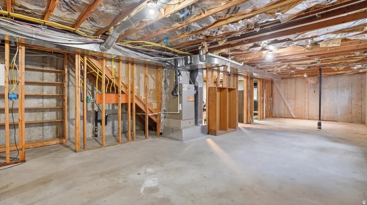 Unfinished basement with concrete flooring, exposed wood framing, and visible utility infrastructure, providing an open canvas for customization