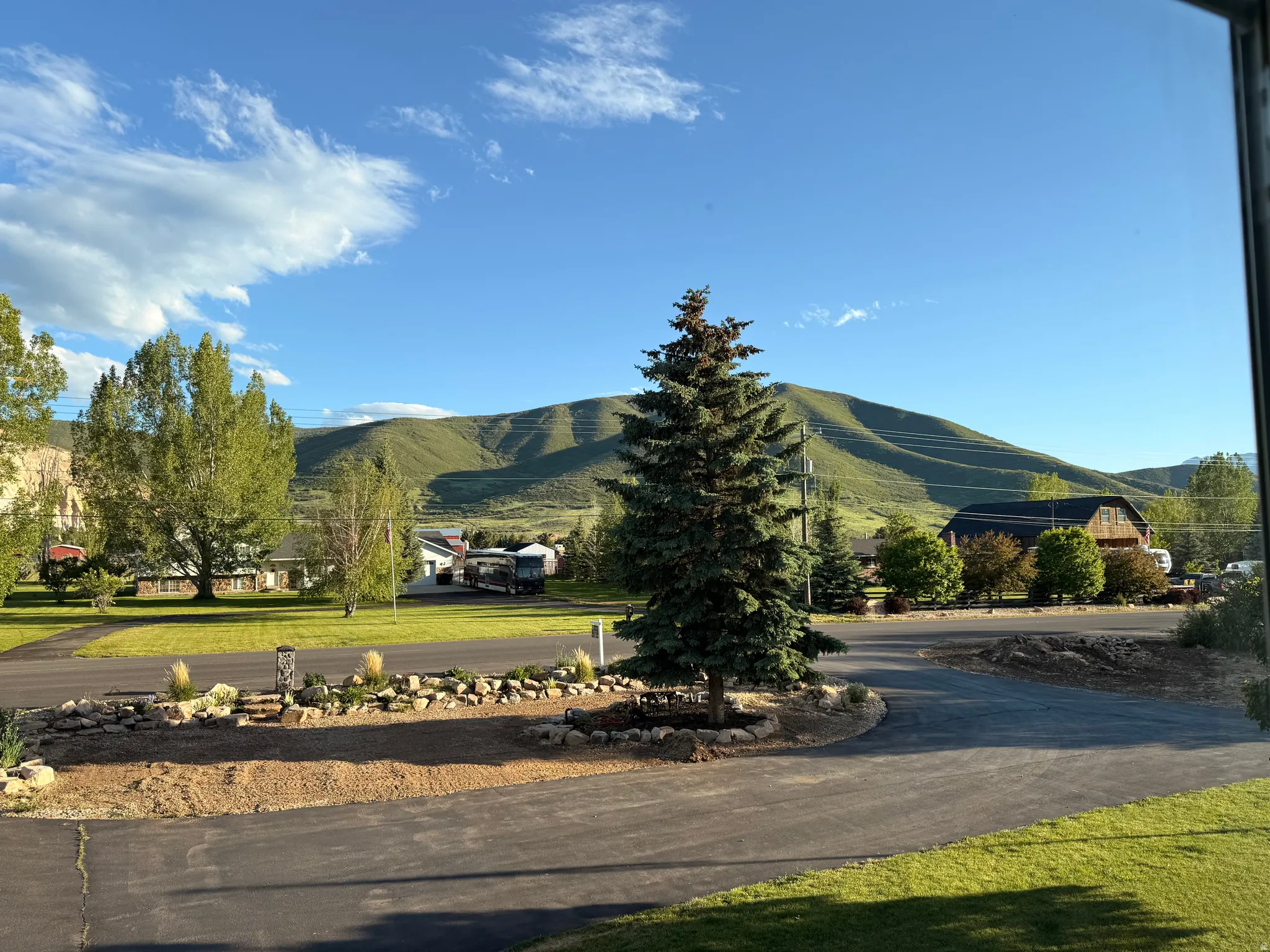 Paved driveway with a central evergreen tree and surrounding rock landscaping