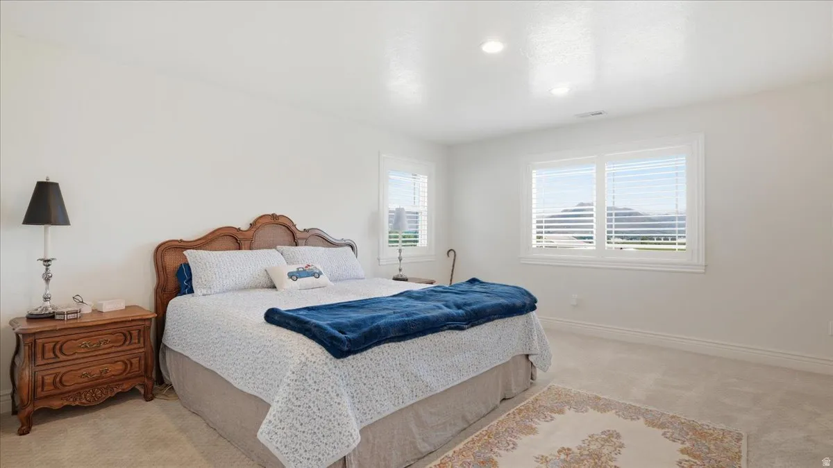 Bright bedroom featuring white walls, recessed lighting, and two windows with white plantation shutters